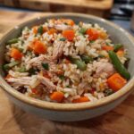 A bowl of Chicken and Rice Dog Food with carrots, peas, and green beans, garnished with herbs.