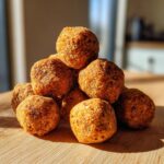 A stack of homemade Chicken & Rice Balls Dog Treats, arranged on a wooden surface in natural sunlight.