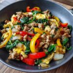 A vibrant Egg and Turkey Power Bowl with colorful bell peppers, spinach, and onions in a white bowl.