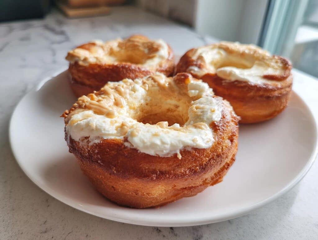 Three peanut butter Dog Donuts Recipe treats on a white plate, topped with white frosting and peanut butter drizzle.