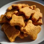 A pile of homemade Peanut Butter Dog Treats shaped like dog bones on a white plate.