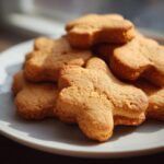 Pile of homemade Peanut Butter Honey Dog Treats shaped like dogs on a white plate, ready to be enjoyed.