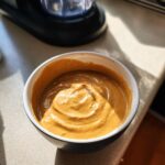 Bowl of creamy peanut butter smoothie for dogs, ready to serve. Blender in background.