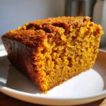 Close-up of a slice of Pumpkin Cake Recipe for Dogs, showing the cake's texture and golden color on a white plate.