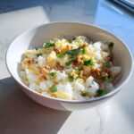 A white bowl filled with a Rice and Egg Bowl DOG RECIPE, garnished with fresh herbs.