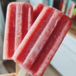 Three homemade Strawberry Banana Frozen Pops for Dogs held in a hand, showing their frosty texture.