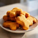 Pile of homemade 3-Ingredient Sweet Potato Dog Cookies shaped like bones on a white plate.