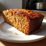 A slice of Sweet Potato and Oatmeal Dog Cake on a white plate, illuminated by natural light.