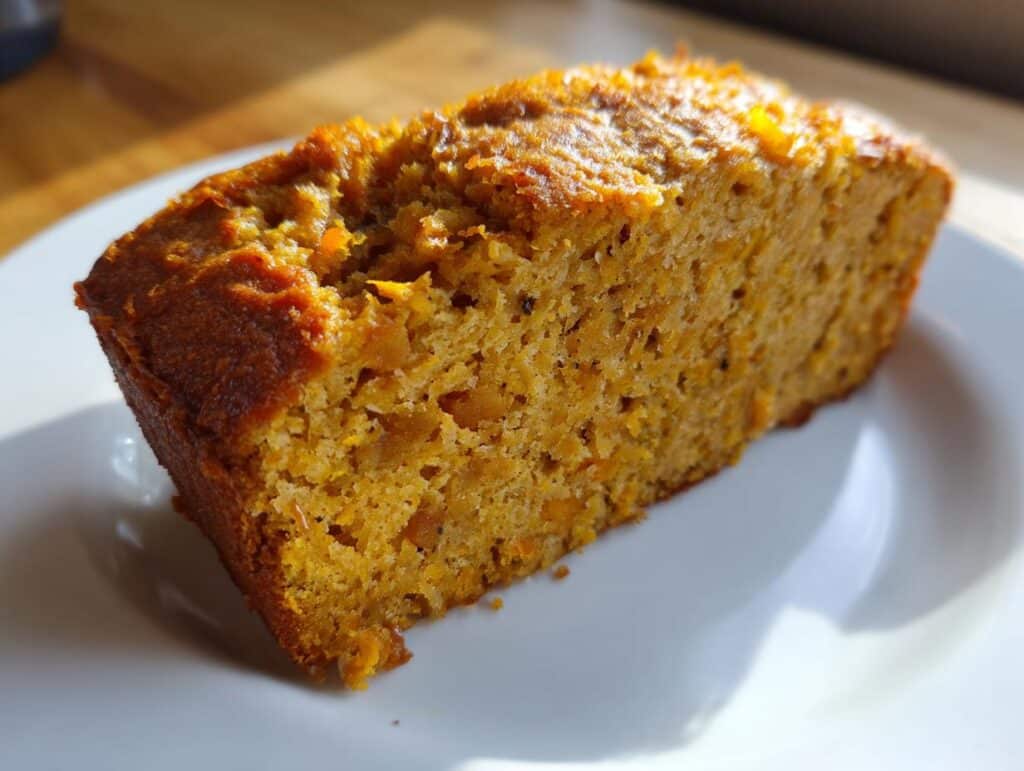 A slice of Sweet Potato and Oatmeal Dog Cake on a white plate, ready to be served to a happy pup.