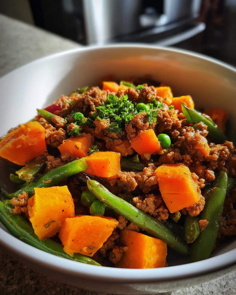 A bowl of homemade Beef & Sweet Potato Vitamin-Rich Dog Food with green beans and peas, garnished with parsley.