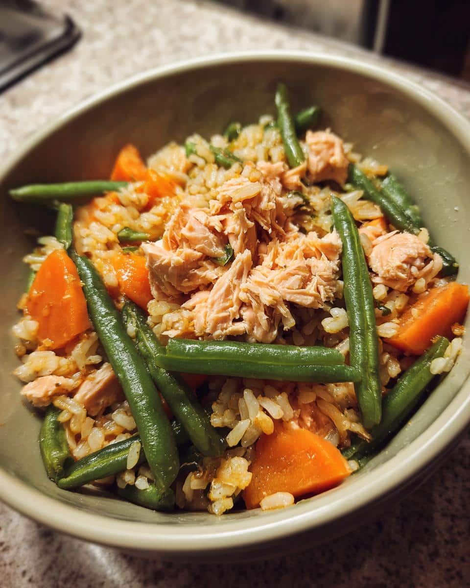 A bowl of Crockpot Salmon & Veggie Dog Dinner, featuring salmon, green beans, carrots, and rice.