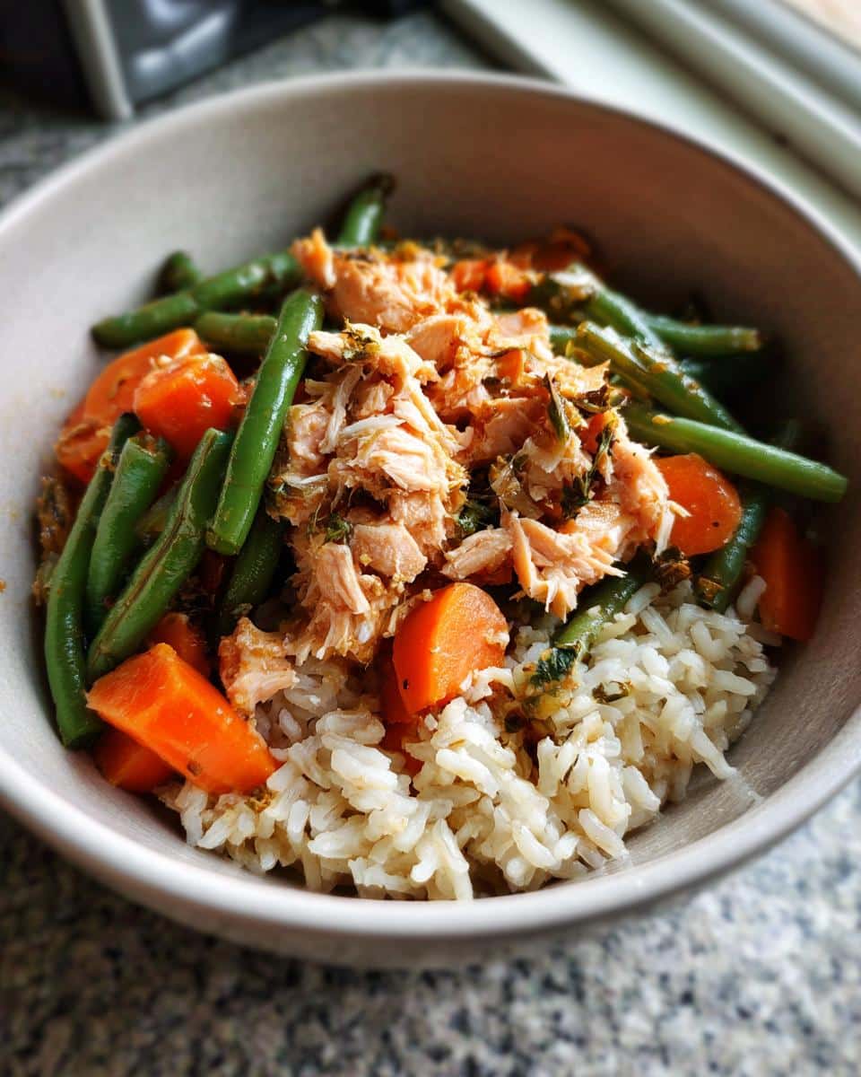 A bowl of Crockpot Salmon & Veggie Dog Dinner, featuring salmon, green beans, carrots, and rice.
