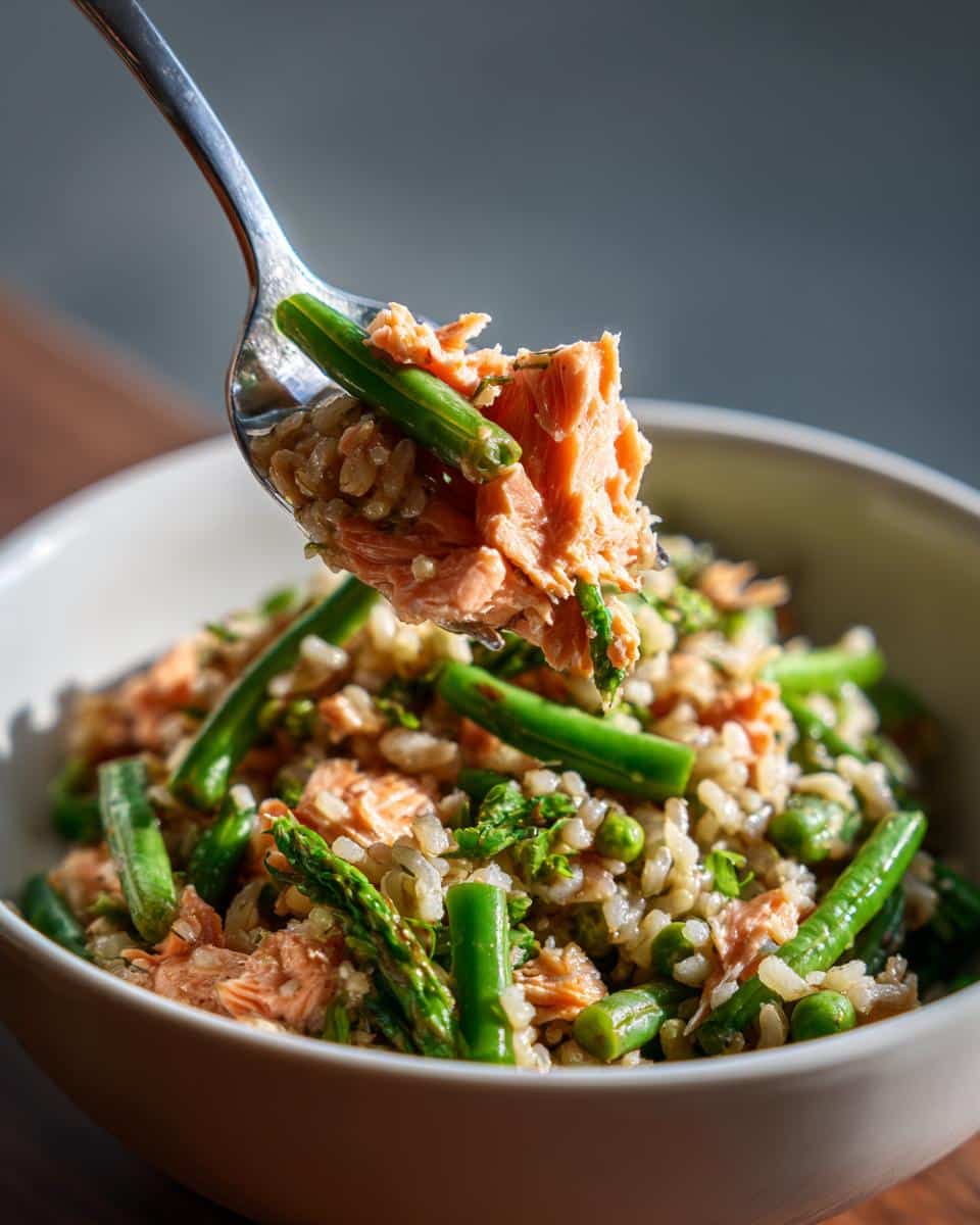 A bowl of Easy Salmon & Green Bean Dog Food with rice, peas, and asparagus, being scooped with a spoon.