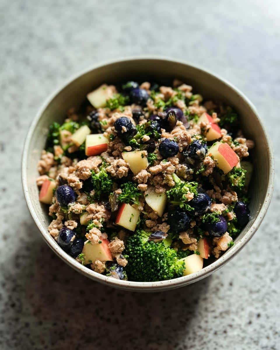 A close-up of a unique Holiday Leftover Turkey Bowl featuring ground meat, blueberries, diced apples, and broccoli florets.