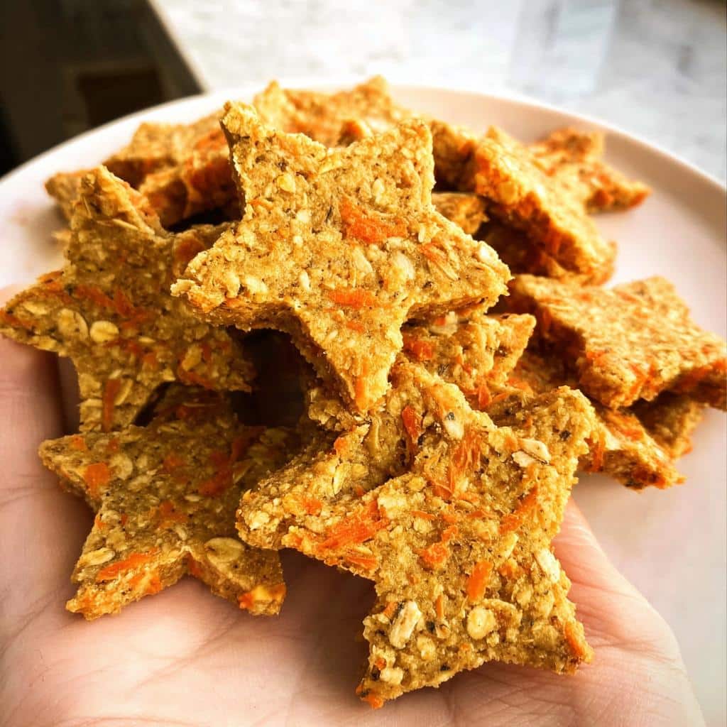A handful of star-shaped Oat Carrot Christmas Pup Biscuits showing visible oats and shredded carrot texture.