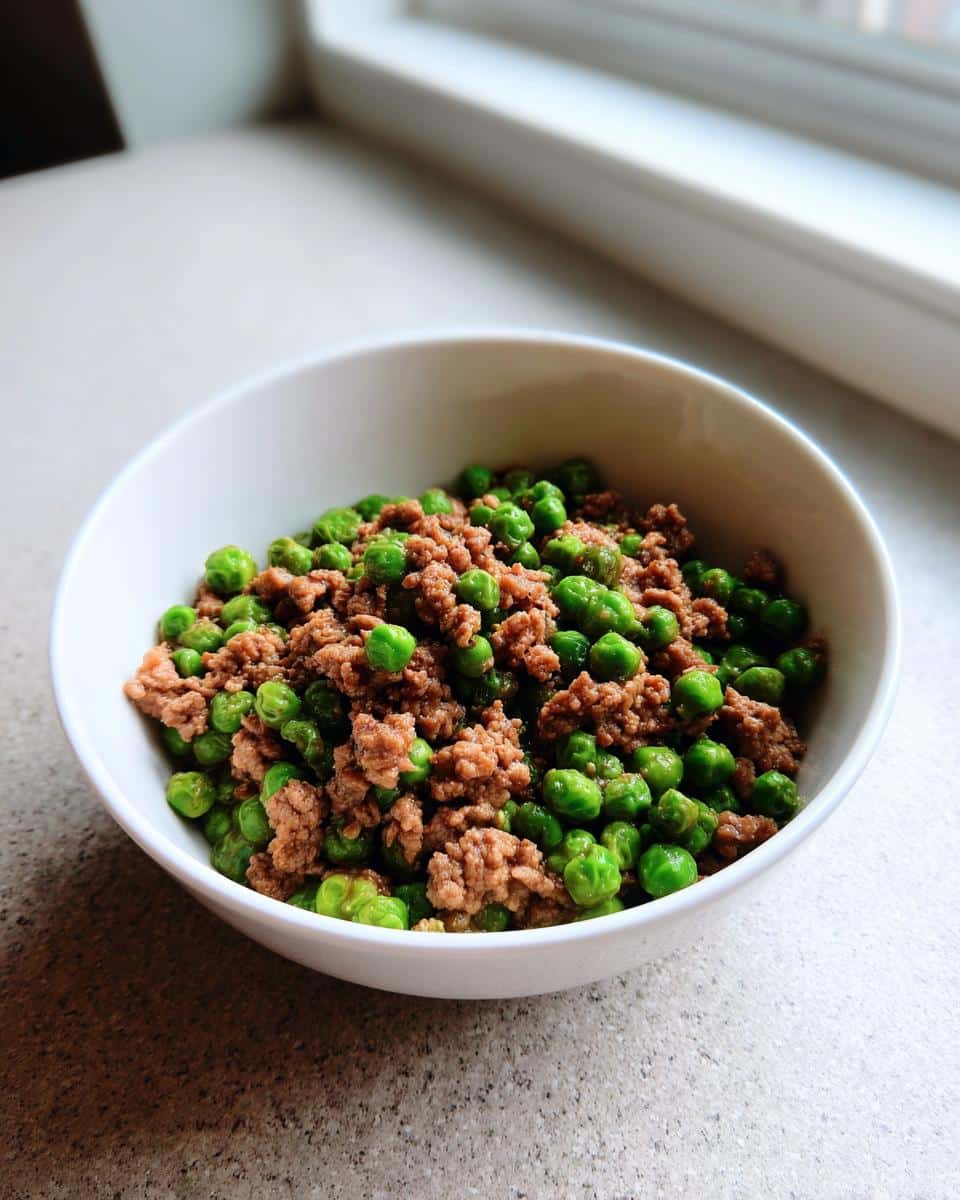 Close-up of cooked ground meat mixed with bright green peas, representing the Rabbit Pea Grain-Free Pup Bowl.