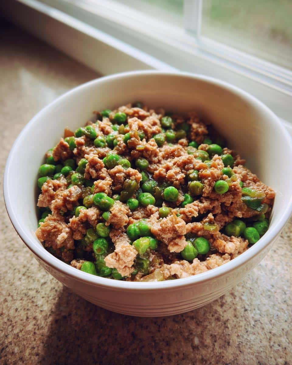 Close-up of a white bowl filled with ground meat and bright green peas, representing the Rabbit Pea Grain-Free Pup Bowl.