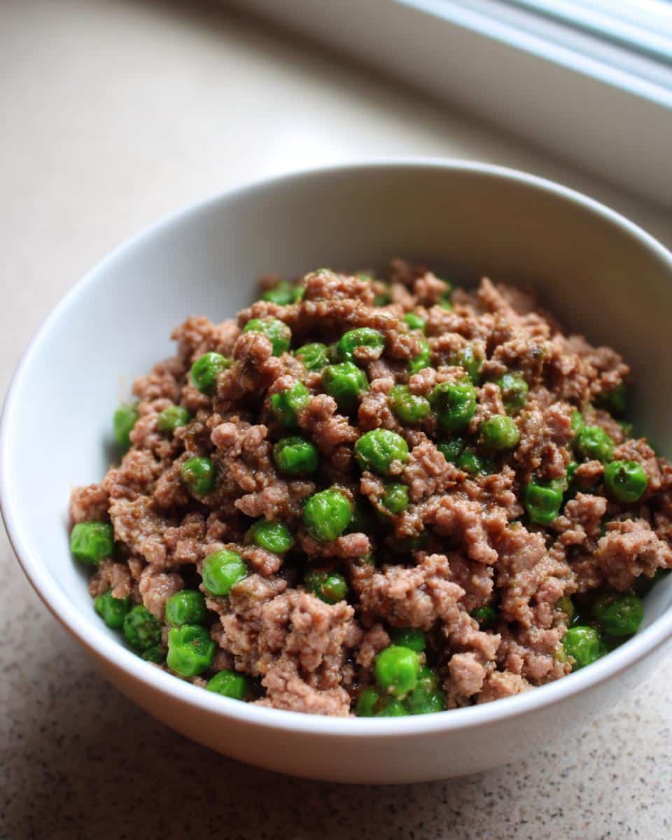 Close-up of a white bowl filled with cooked ground rabbit meat mixed with bright green peas for a Rabbit Pea Grain-Free Pup Bowl.