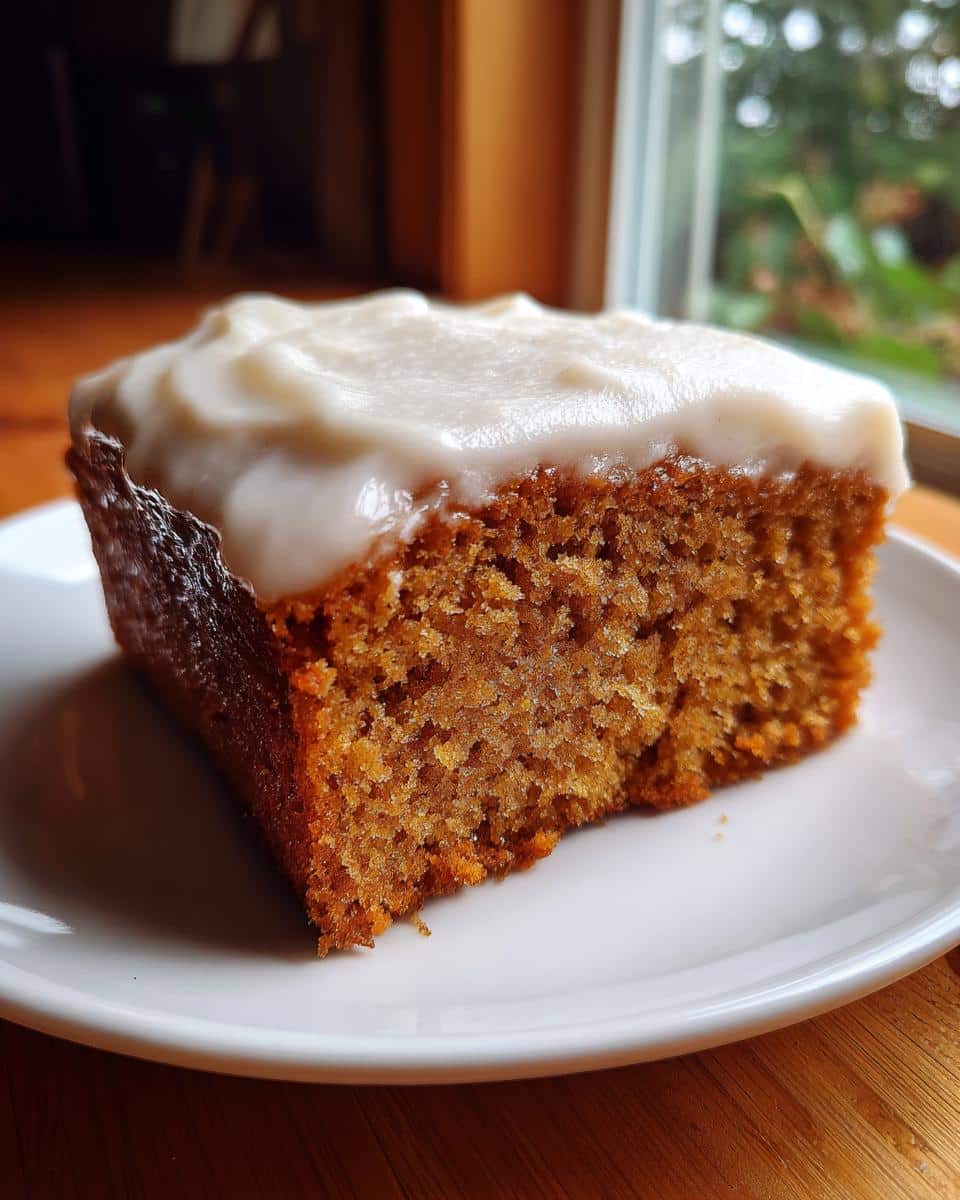 Close-up of a moist slice of Apple Cinnamon Dog Cake topped with thick white frosting, served on a white plate.