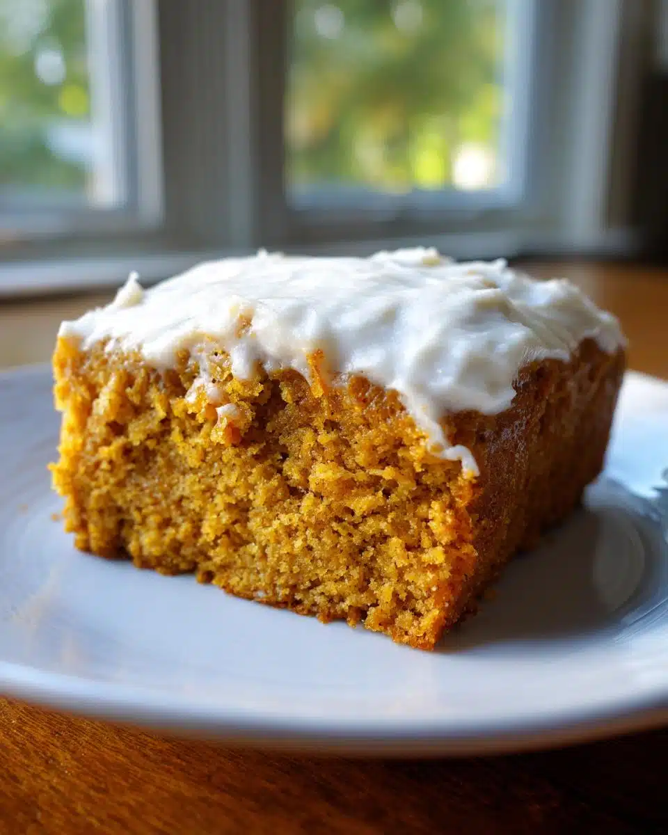 Close-up of a moist slice of Apple Cinnamon Dog Cake topped with thick white frosting on a white plate.