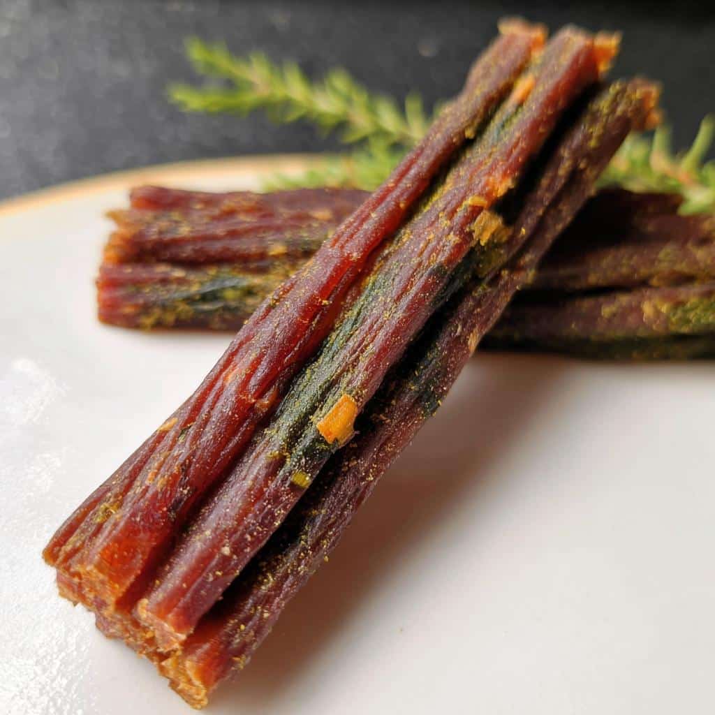 Close-up of seasoned Beef and Vegetable Chew Sticks, featuring dark red meat texture and green/orange vegetable specks.