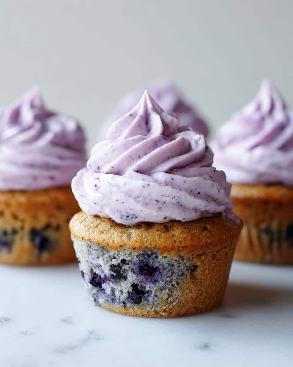 Close-up of a single blueberry yogurt pupcake topped with swirled purple frosting, featuring visible blueberries in the cake base.