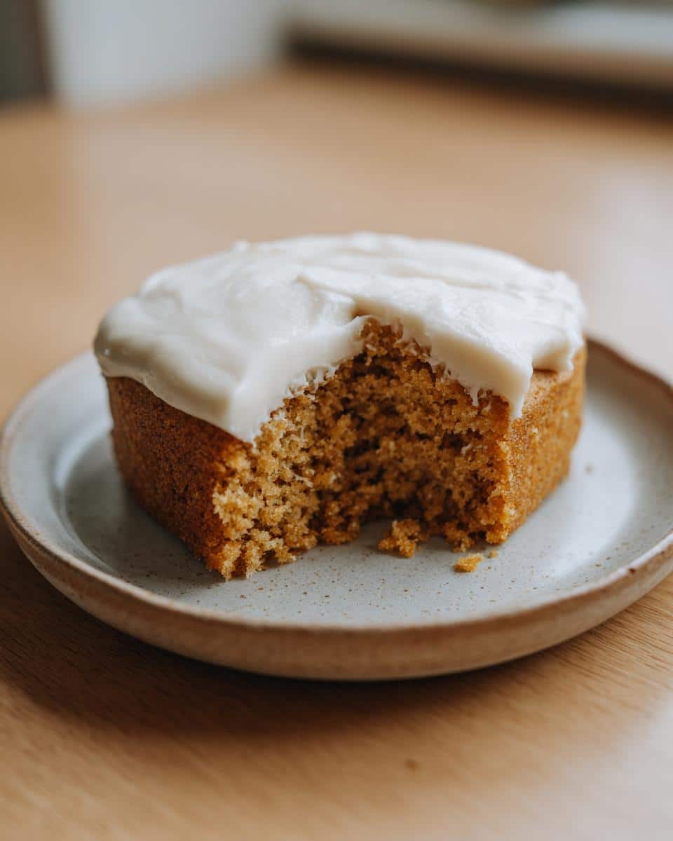 Close-up of a square slice of Coconut and Honey Dog Cake with white frosting, showing a bite taken out.