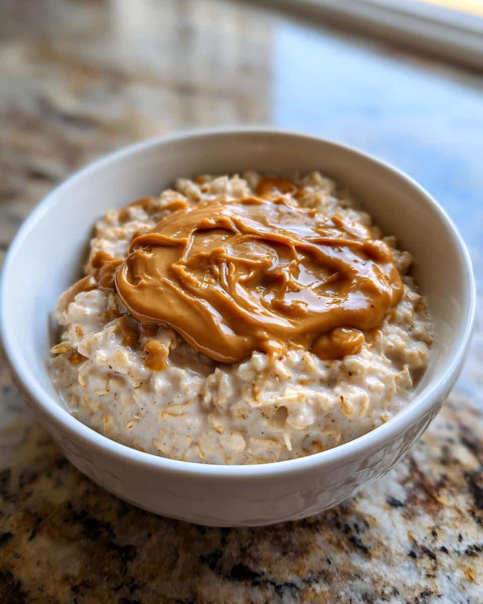 Close-up of creamy peanut butter oatmeal topped with a generous swirl of melted peanut butter in a white bowl.