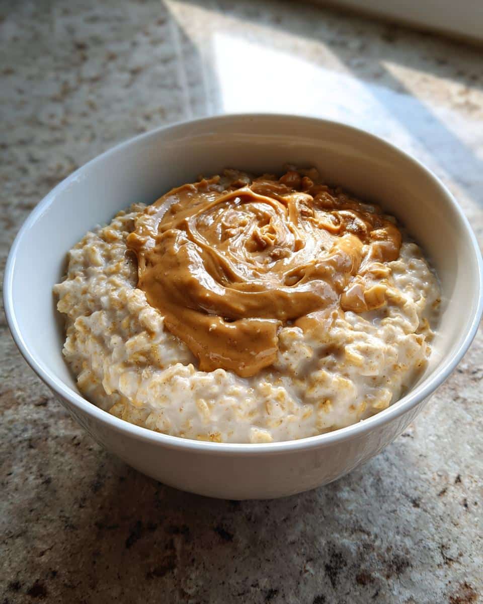 Close-up of creamy peanut butter oatmeal topped with a swirl of melted peanut butter in a white bowl.