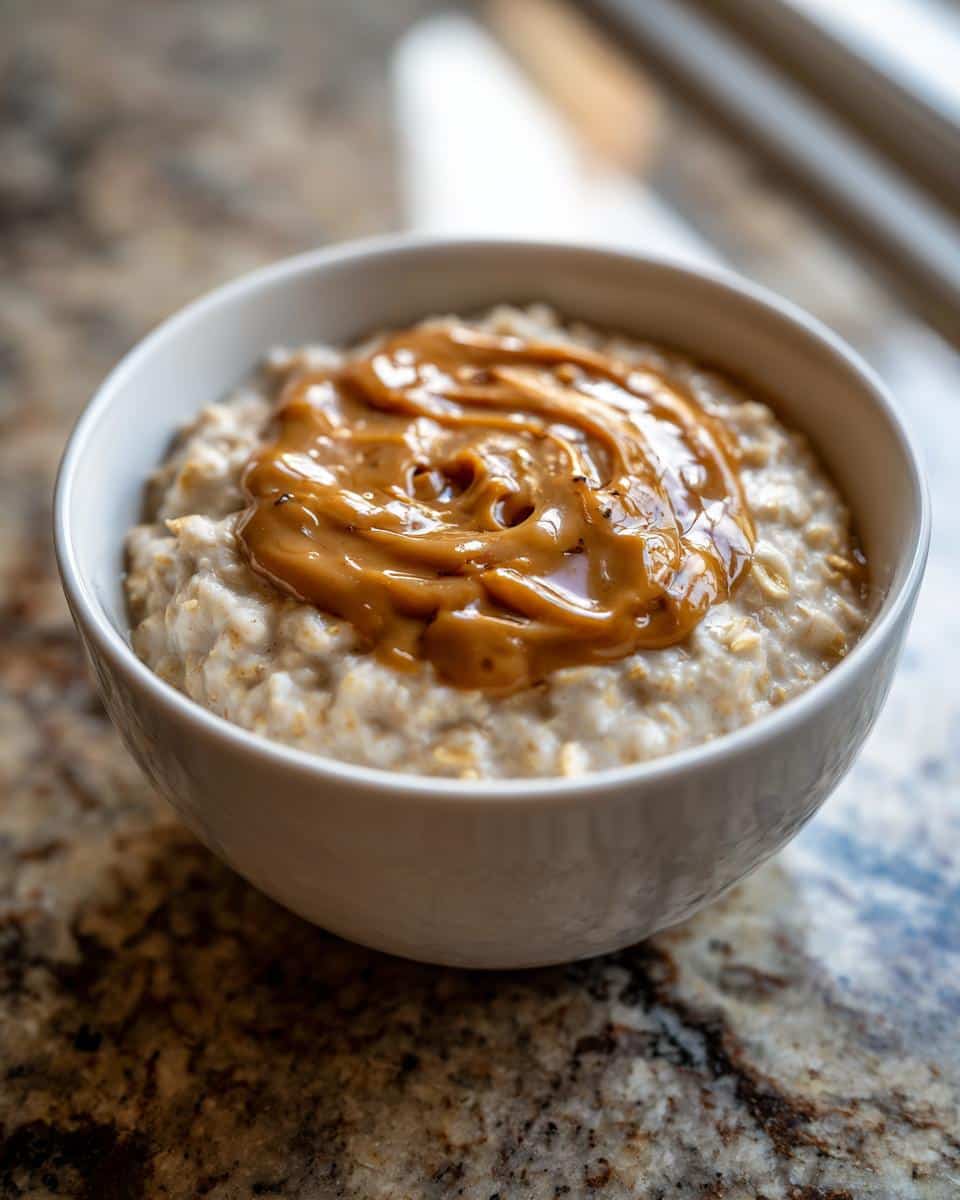 Close-up of creamy peanut butter oatmeal topped with a swirl of melted peanut butter in a white bowl.