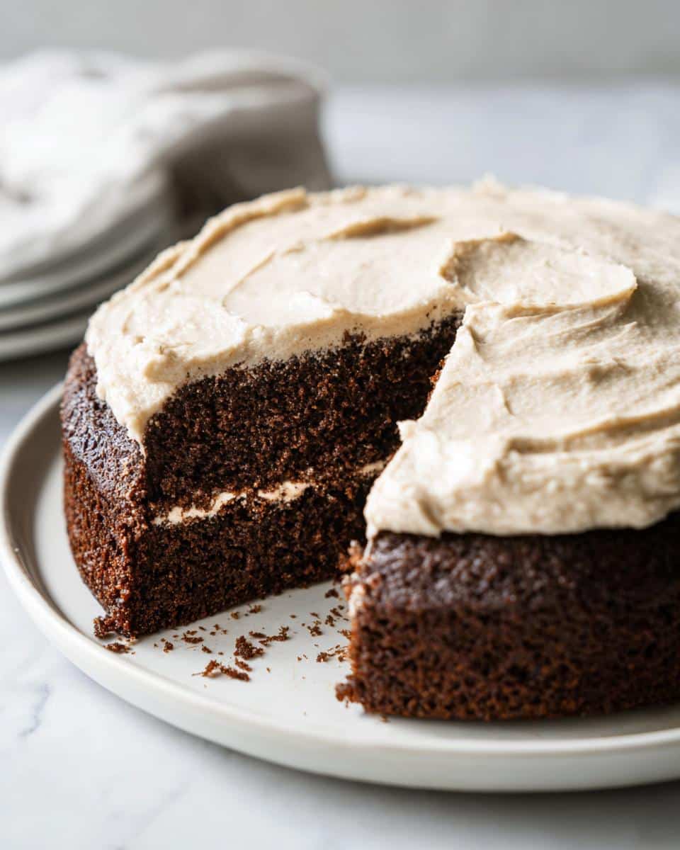 A rich, dark layer of Homemade Peanut Butter Dog Cake with a thick layer of light brown frosting, one slice removed.