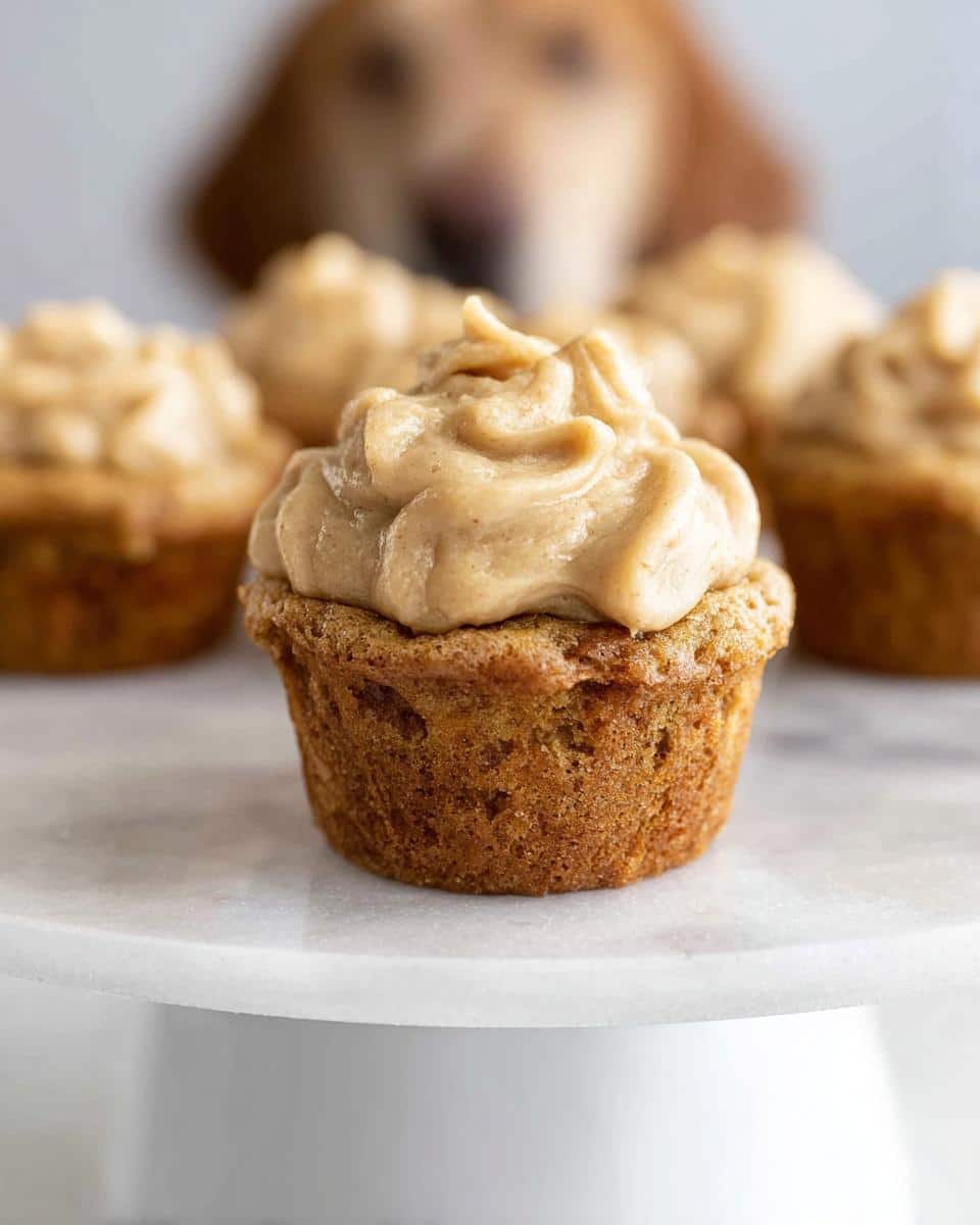 A close-up of one Mini Pupcake with Peanut Butter & Banana frosting, with a dog looking on in the background.