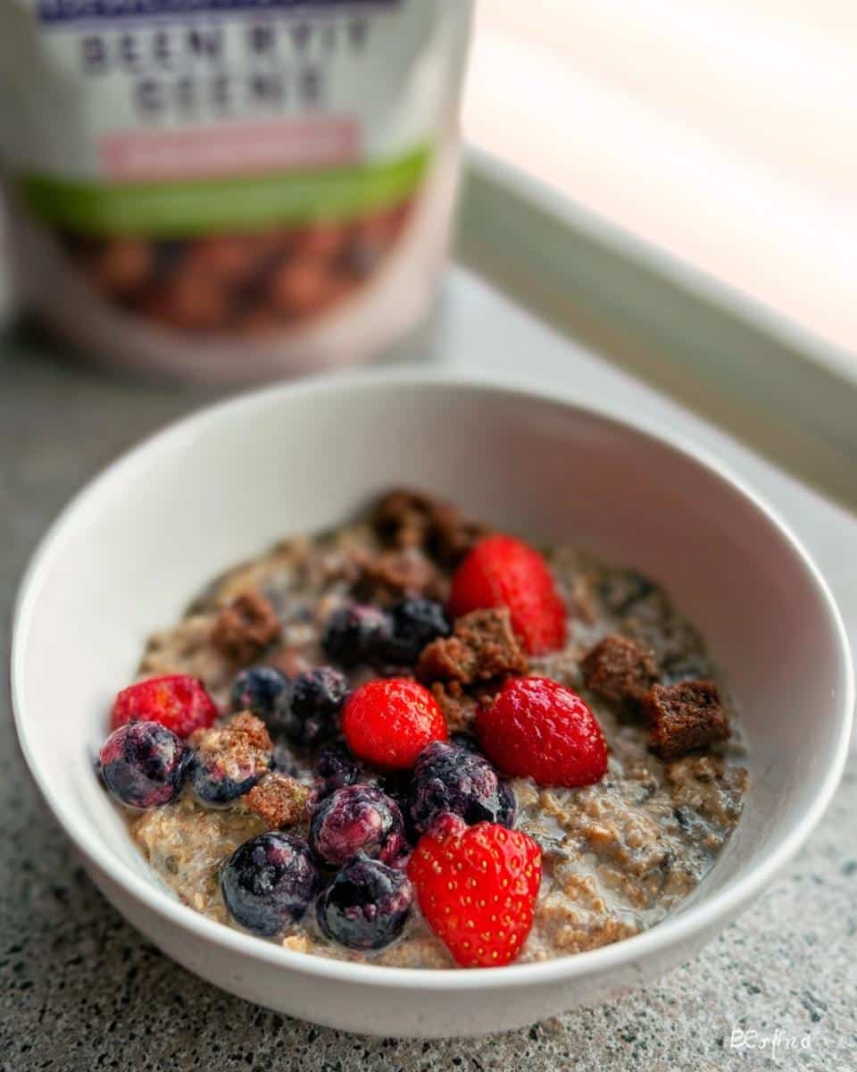 Close-up of a bowl of Oatmeal Dog topped with fresh strawberries, blueberries, and crunchy brown cereal pieces.