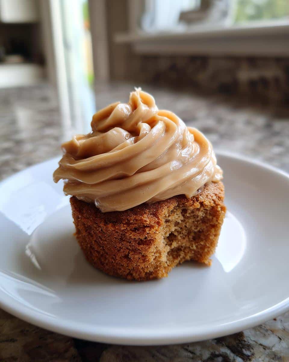 Close-up of a Peanut Butter Frosted Pupcake with a bite taken out, sitting on a white plate.