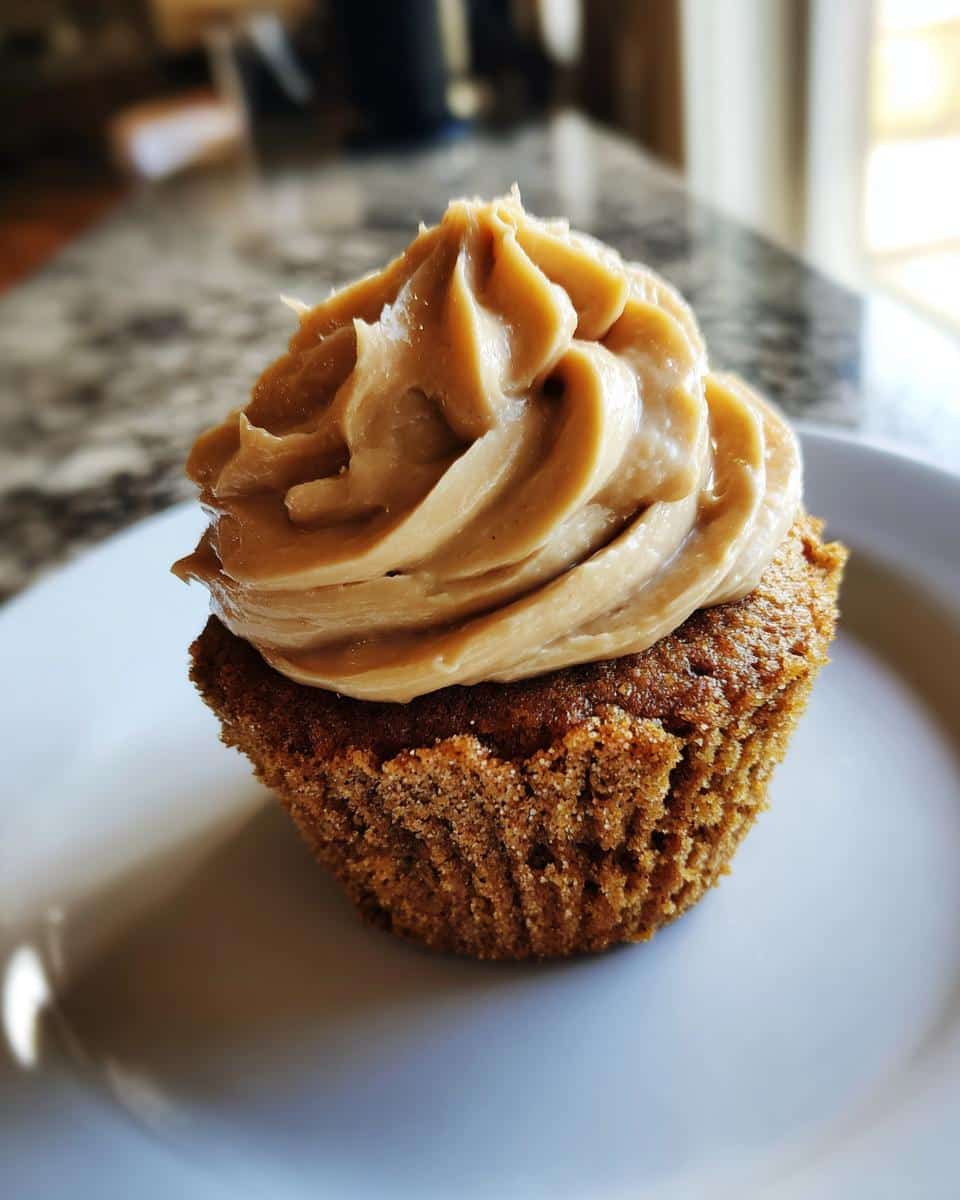 A single, delicious Peanut Butter Frosted Pupcake with thick, swirled frosting, sitting on a white plate.