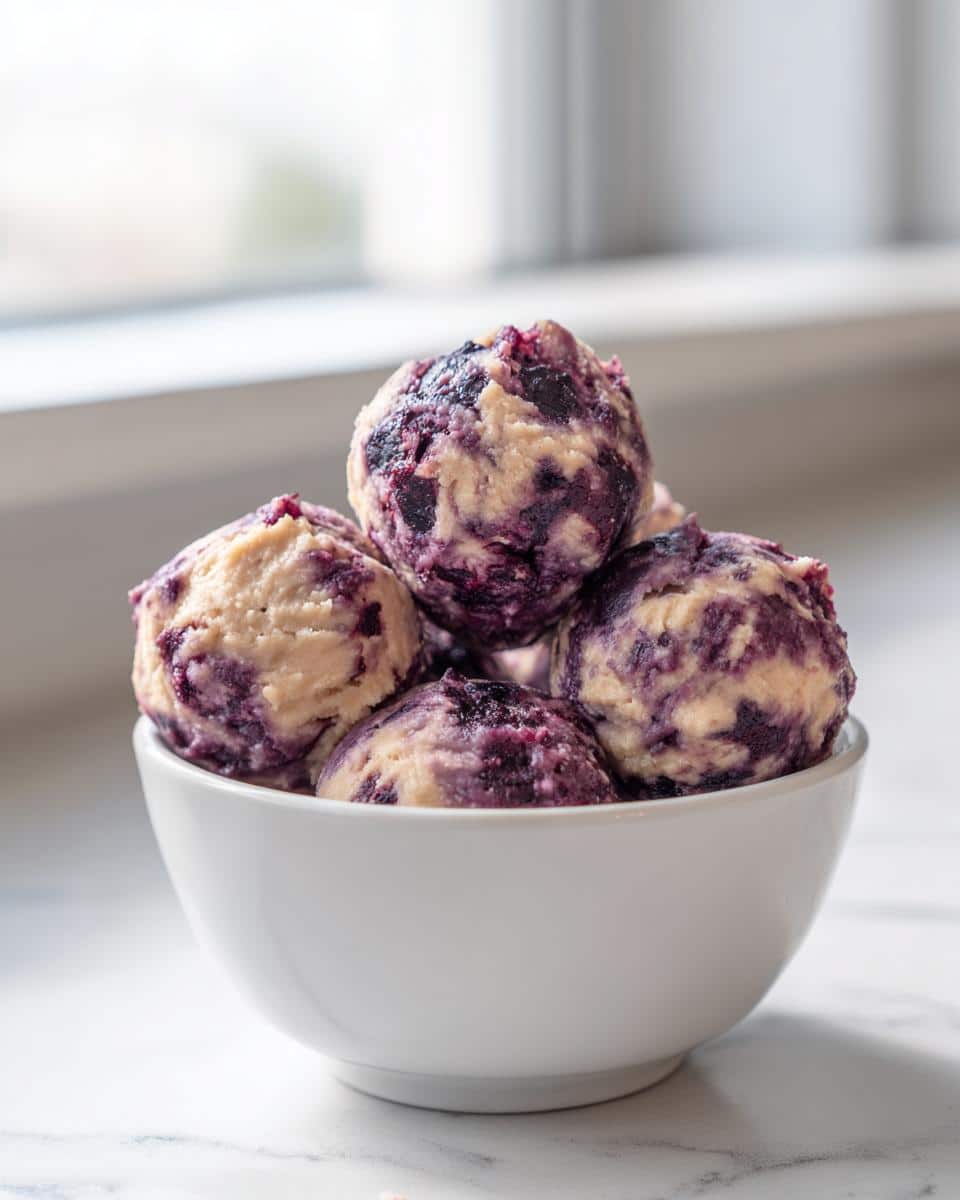 A white bowl filled with scoops of Blueberry & Peanut Butter Frozen Swirl Bites for Dogs, swirled with purple blueberry.