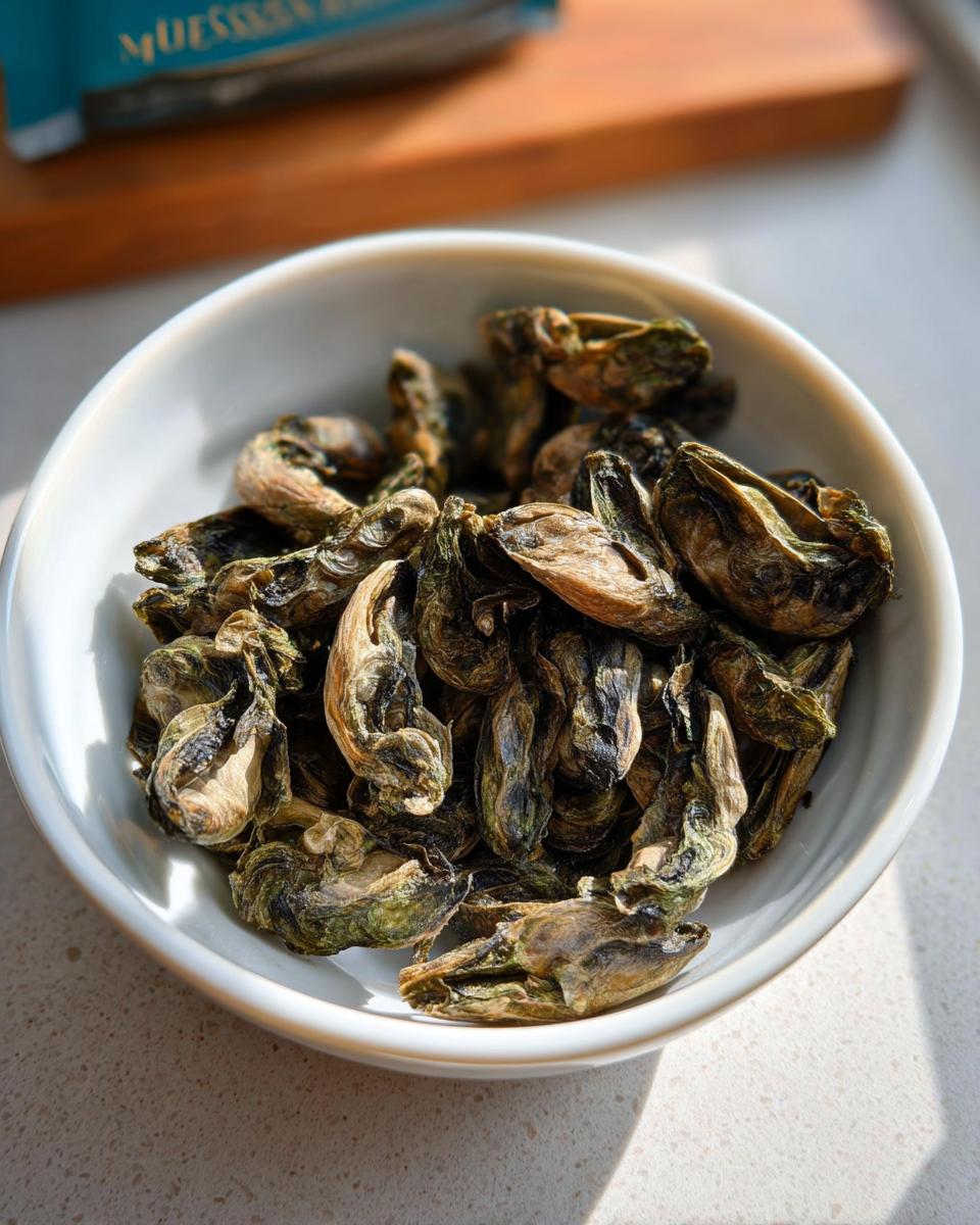 A white bowl filled with dried Green Lipped Mussel Bites, showing their shriveled, greenish-brown appearance.