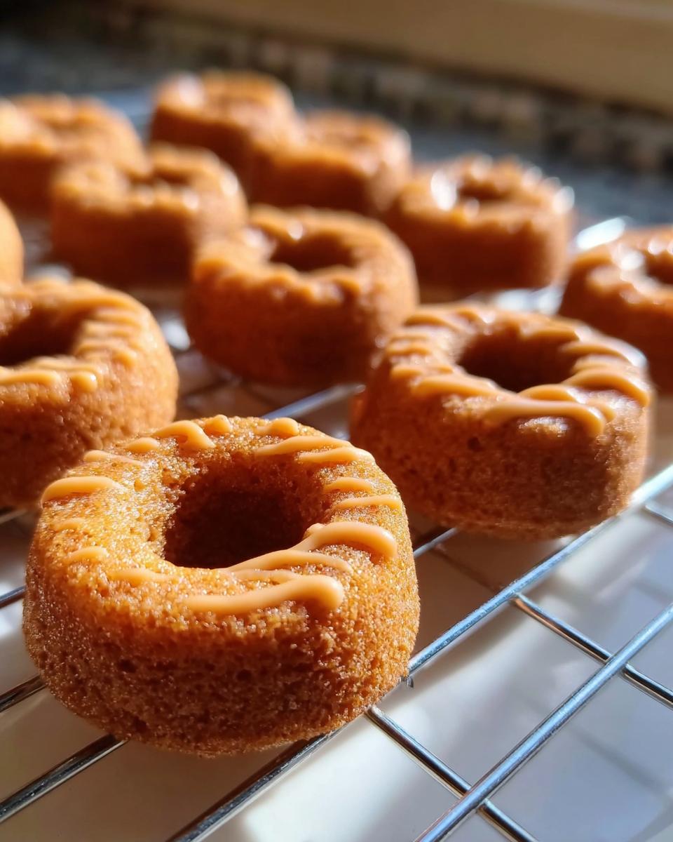 Close-up of freshly baked Peanut Butter & Pumpkin Pup Donuts cooling on a wire rack with light glaze.