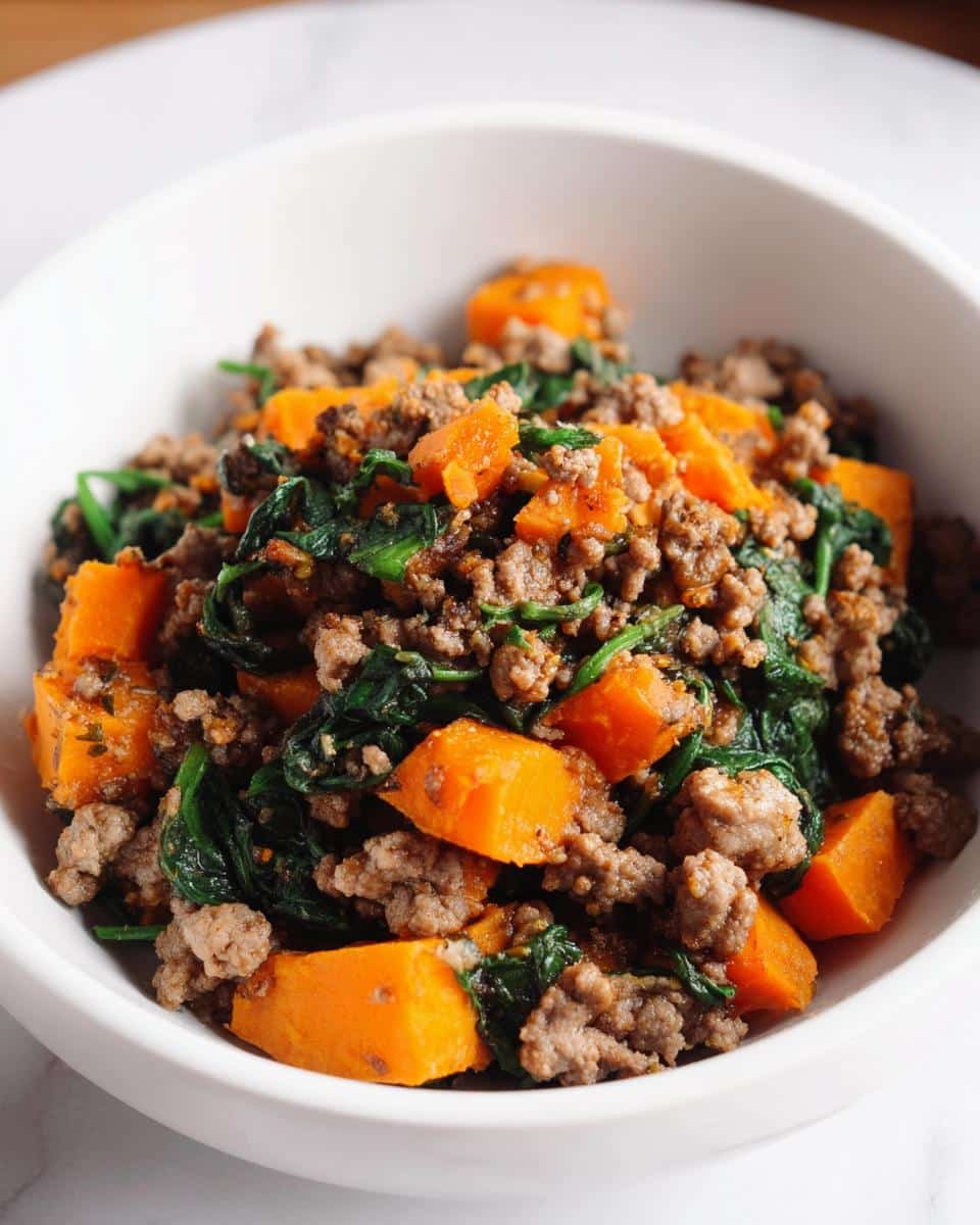 Close-up of homemade dog food featuring ground beef, bright orange sweet potato chunks, and dark green spinach.