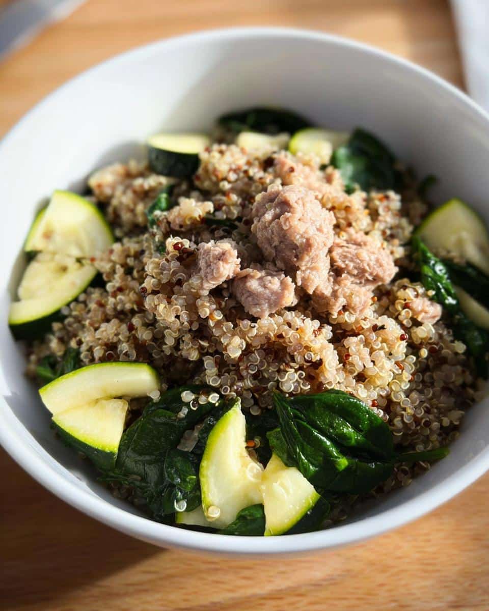 Close-up of a white bowl containing quinoa, ground meat, spinach, and sliced zucchini, suitable for DIY dog food for diabetic dogs.