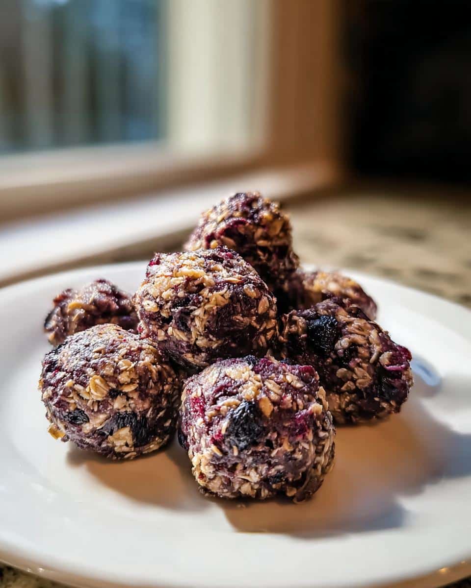 Close-up of homemade dog treats made with venison, oatmeal & blueberries, rolled into small balls on a white plate.