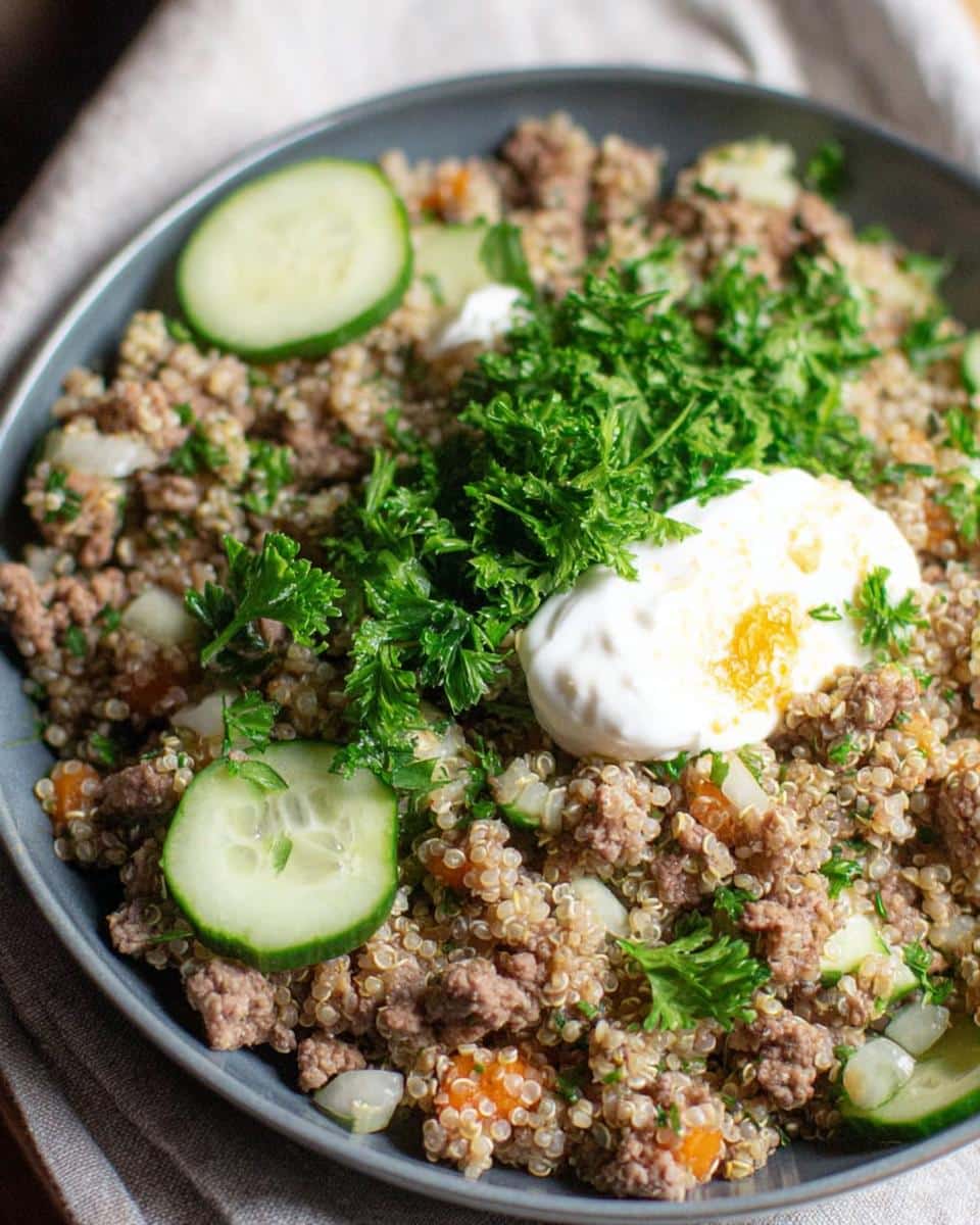 A close-up of a bowl filled with a homemade dog food recipe featuring lamb, quinoa, carrots, cucumber, and parsley.